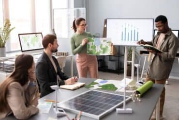 Team members collaborate in an office setting, highlighting a solar panel as part of their sustainable management efforts.