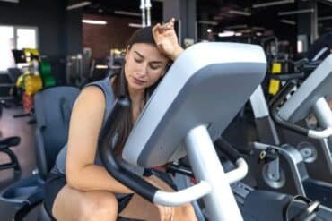 Tired woman sitting on an exercise bike in a gym, resting after an intense workout session.