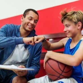 A man and a boy sit together in a gym, holding a basketball and enjoying their time on the court.