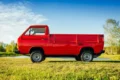 A red 1997 Subaru Sambar Truck V-KS4 4WD parked in a grassy field under a clear blue sky.
