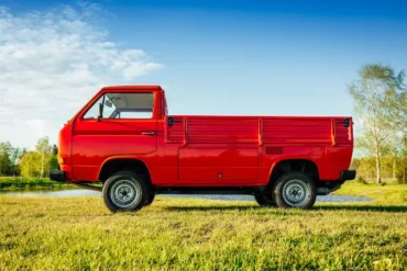 A red 1997 Subaru Sambar Truck V-KS4 4WD parked in a grassy field under a clear blue sky.