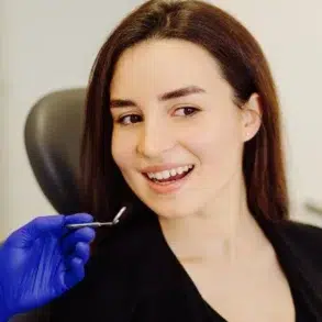 A close-up of a person in a black shirt sitting in a clinic, receiving a cosmetic treatment from a gloved hand.