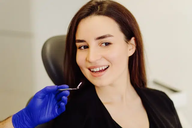 A close-up of a person in a black shirt sitting in a clinic, receiving a cosmetic treatment from a gloved hand.