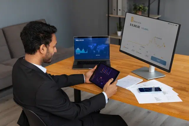 Man in a business suit sitting at a desk with a laptop and tablet, focused on cloud-based synchronization for traders.