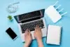 A woman typing on a laptop, with a phone and notebook beside her, focused on comparing internet service options.