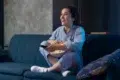 A woman seated on a couch holds a bowl of popcorn, engaged with HD Hub 4 U Streaming.