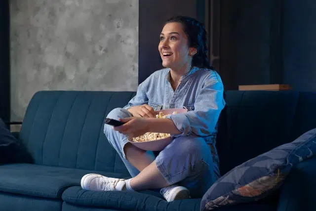 A woman seated on a couch holds a bowl of popcorn, engaged with HD Hub 4 U Streaming.