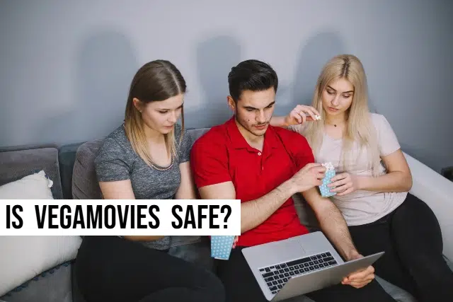 Three people sitting on a couch, focused on a laptop, discussing the safety of Vegamovies.