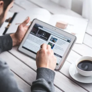 Man using a tablet on a wooden table to check the latest updates on QuikerNews.com.