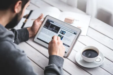 Man using a tablet on a wooden table to check the latest updates on QuikerNews.com.