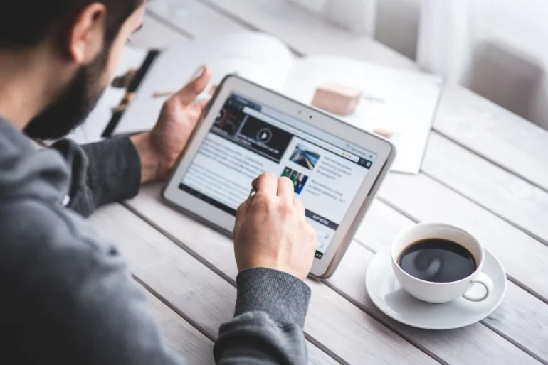 Man using a tablet on a wooden table to check the latest updates on QuikerNews.com.