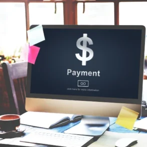 A desktop computer displaying a payment screen with a dollar sign, surrounded by a coffee cup and colorful sticky notes on a desk.