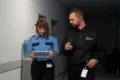 A security officer and a staff member walk down a hallway, reviewing information on a tablet in a professional setting.