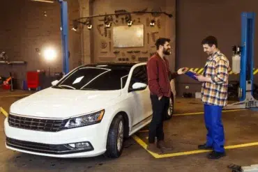 A tech-savvy mechanic discusses diagnostics with a customer beside a modern white car in a repair shop.