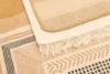 Close-up of layered rugs in earthy tones with geometric patterns and fringed edges, creating a cozy and textured interior design.