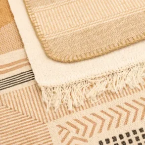 Close-up of layered rugs in earthy tones with geometric patterns and fringed edges, creating a cozy and textured interior design.