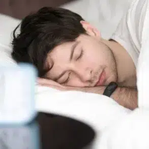 A person lies comfortably in bed, resting with their arm tucked under a pillow, a blue alarm clock visible on the nightstand.