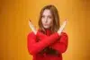 A woman in a red sweater gestures with crossed arms against a bright yellow background, conveying a message of rejection or defiance.