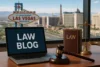 A laptop displaying "LAW BLOG" sits on a desk with legal books and a gavel, overlooking the Las Vegas skyline.