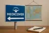 A blue sign with "MEDICOVER" and an arrow points left, set against a world map and a notebook with a pen on a wooden table.