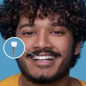 A person with curly hair wearing a yellow shirt, posing against a bright blue background, with an earbud visible.