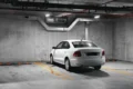 A parked white sedan in a dimly lit, concrete parking garage with distinct parking lines.