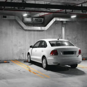 A parked white sedan in a dimly lit, concrete parking garage with distinct parking lines.