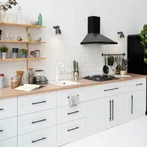 Bright modern kitchen featuring white cabinets, wooden countertop, gas stove, and a black fridge, adorned with plants and stylish decor.