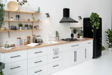 Bright modern kitchen featuring white cabinets, wooden countertop, gas stove, and a black fridge, adorned with plants and stylish decor.