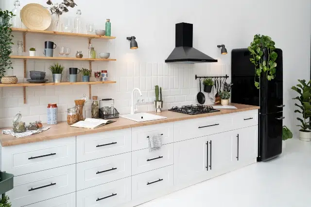 Bright modern kitchen featuring white cabinets, wooden countertop, gas stove, and a black fridge, adorned with plants and stylish decor.