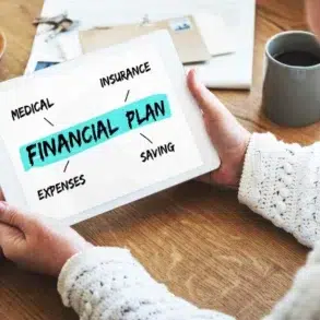 A person holds a tablet displaying a financial plan, outlining medical, insurance, expenses, and saving strategies on a wooden table.
