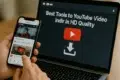 A person holding a smartphone displays YouTube, while a laptop screen shows "Best Tools to Download YouTube Videos in HD Quality."
