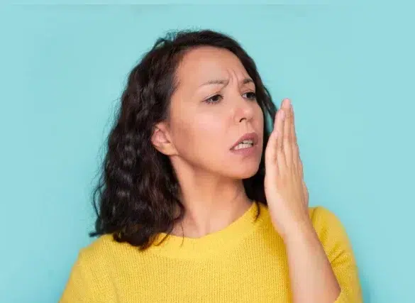 A person with curly hair wears a bright yellow sweater and gestures with their hand against a teal background.