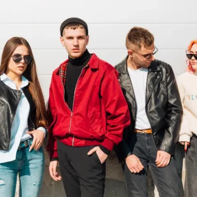Four stylish young adults stand together, showcasing trendy outfits against a bright, minimalist background.