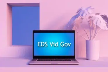 A laptop displaying "EDS Vid Gov" on a blue background, with a minimalist interior featuring a plant and a geometric window.