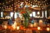 A beautifully arranged table with flowers, candles, and soft lighting, set in a cozy barn with twinkling overhead lights.