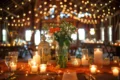 A beautifully arranged table with flowers, candles, and soft lighting, set in a cozy barn with twinkling overhead lights.