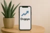 A smartphone displaying the app "Ovppyo" with an upward arrow symbol, placed beside a potted plant on a wooden table.