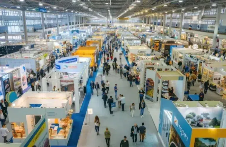 Aerial view of a busy trade exhibition hall filled with colorful booths and crowds of attendees exploring various displays.
