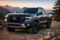 A black Nissan pickup truck parked on rocky terrain, with mountains and trees in the background under a sunset sky.
