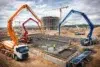 Construction site featuring concrete trucks with boom arms pouring concrete into a foundation. Workers and cranes are visible.