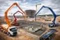 Construction site featuring concrete trucks with boom arms pouring concrete into a foundation. Workers and cranes are visible.