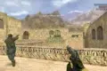 Video game screenshot from a desert map in Counter-Strike. Players aim guns in a tense combat scene with stone walls and mountain backdrop.