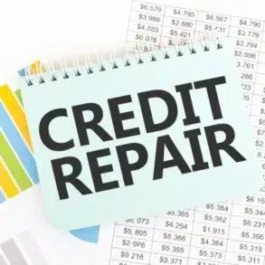A notepad with "CREDIT REPAIR" written in bold on top of financial charts and spreadsheets showing various dollar amounts.