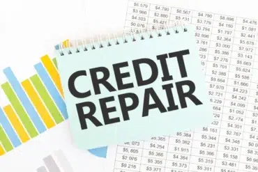 A notepad with "CREDIT REPAIR" written in bold on top of financial charts and spreadsheets showing various dollar amounts.