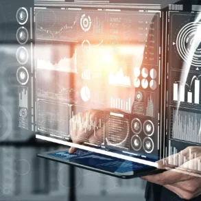 A person holds a tablet displaying a glowing virtual interface with graphs, charts, and data visualizations, conveying a futuristic and analytical tone.