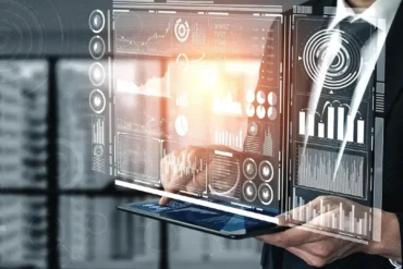 A person holds a tablet displaying a glowing virtual interface with graphs, charts, and data visualizations, conveying a futuristic and analytical tone.