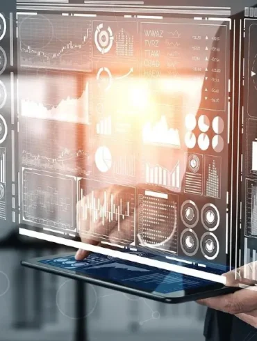 A person holds a tablet displaying a glowing virtual interface with graphs, charts, and data visualizations, conveying a futuristic and analytical tone.