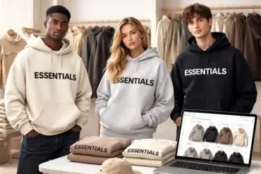 Three models wearing "ESSENTIALS" hoodies in beige, grey, and black, surrounded by clothes and a laptop displaying similar apparel. Casual, trendy vibe.