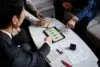 A group of professionals in suits collaborates over a tablet displaying graphs, surrounded by documents and a calculator on a table.